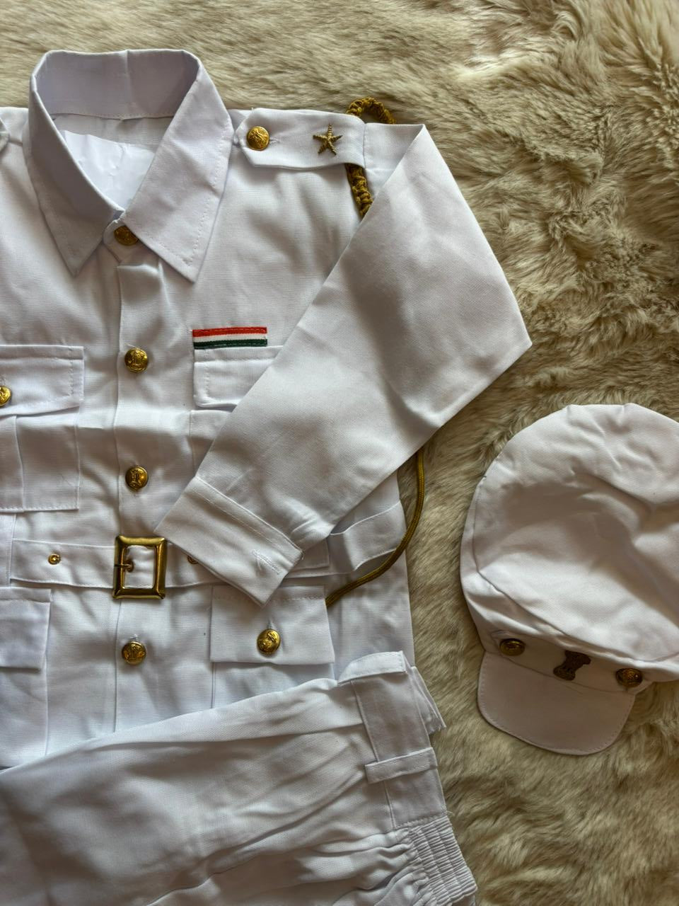 White uniform shirt with gold buttons, white cap, and white pants on a textured beige surface.